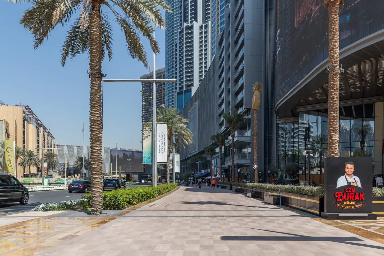 A paved pedestrian walkway runs alongside modern high-rise buildings and palm trees.