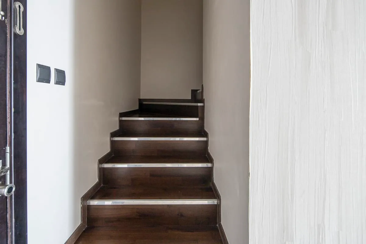 A dark wooden staircase rises between light-colored walls.