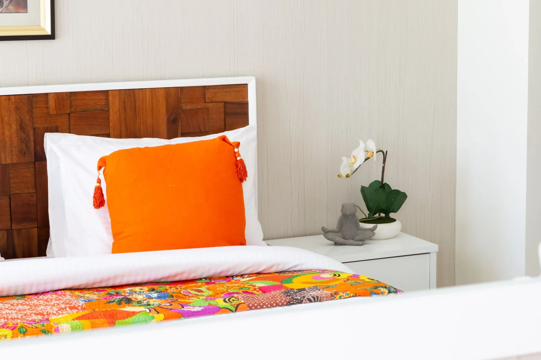 Bedroom with a wooden headboard, bright orange pillow, and colorful bedspread.