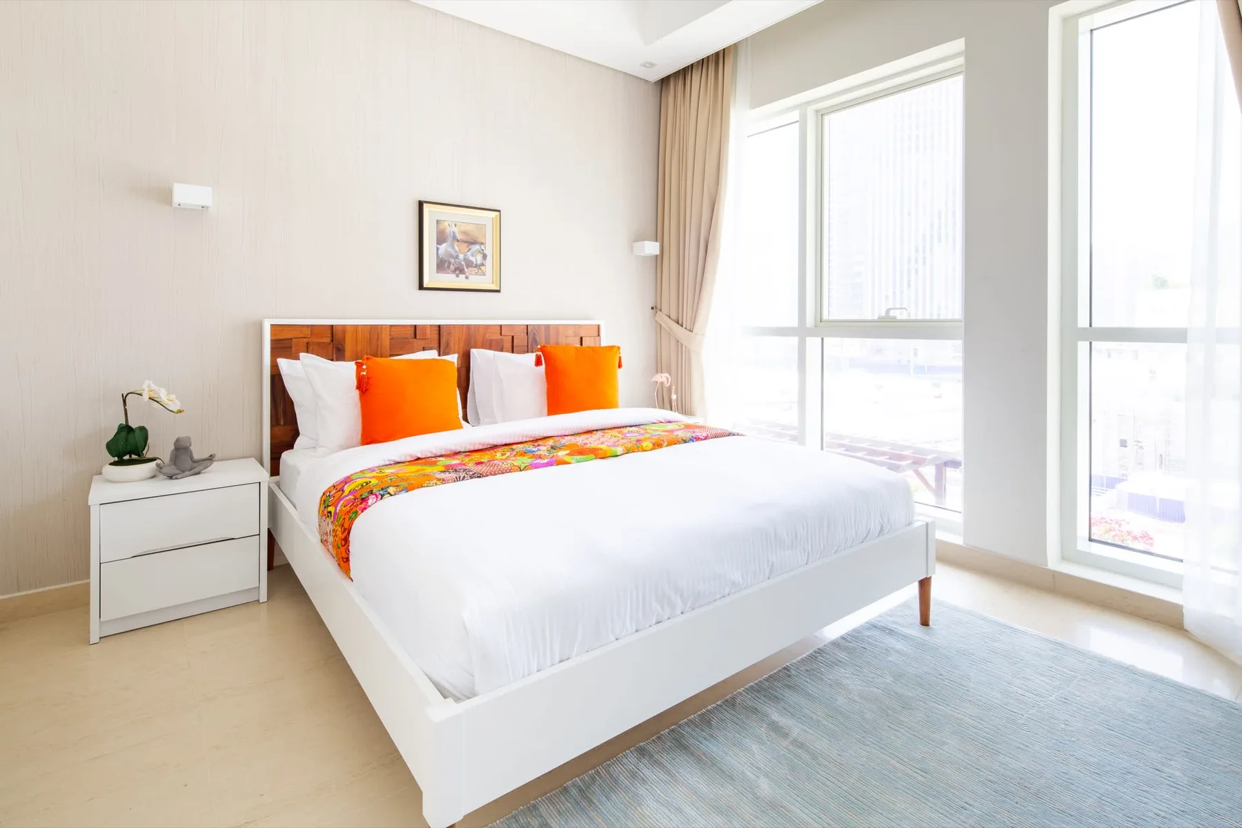 A bright bedroom with a white bed, colorful pillows, and tall windows.