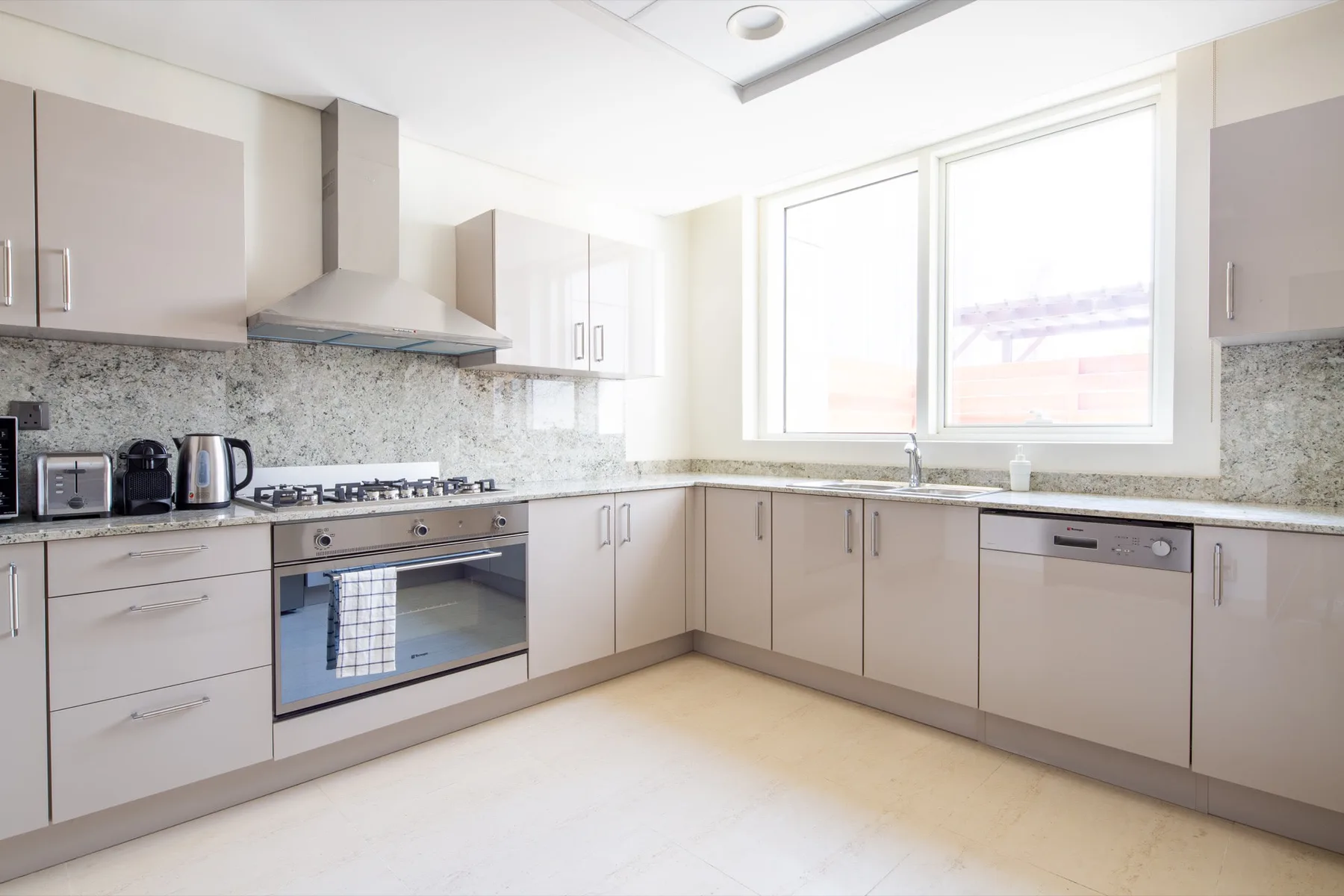 A bright kitchen with pale cabinets, a tiled backsplash, and a large window.