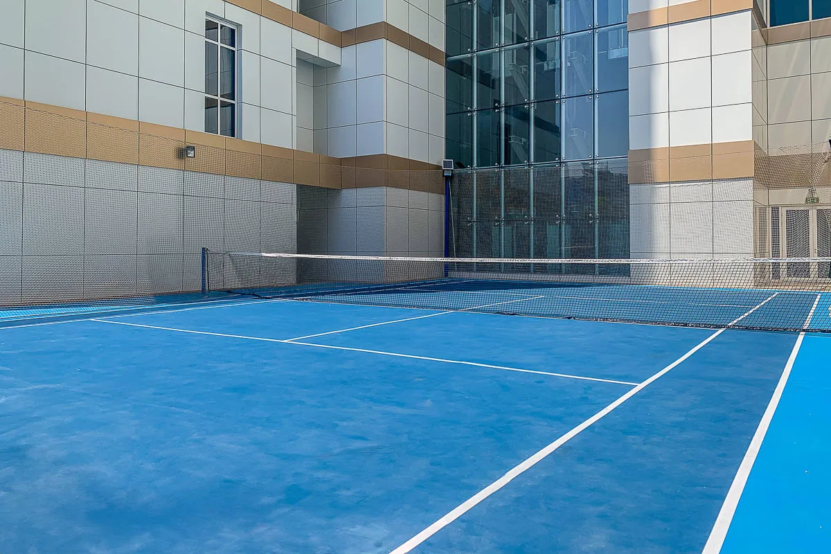 A blue outdoor court with white boundary lines beside a modern building.