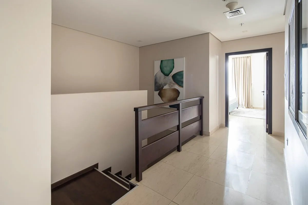 A bright indoor hallway opens onto a stairwell, with abstract wall art nearby.