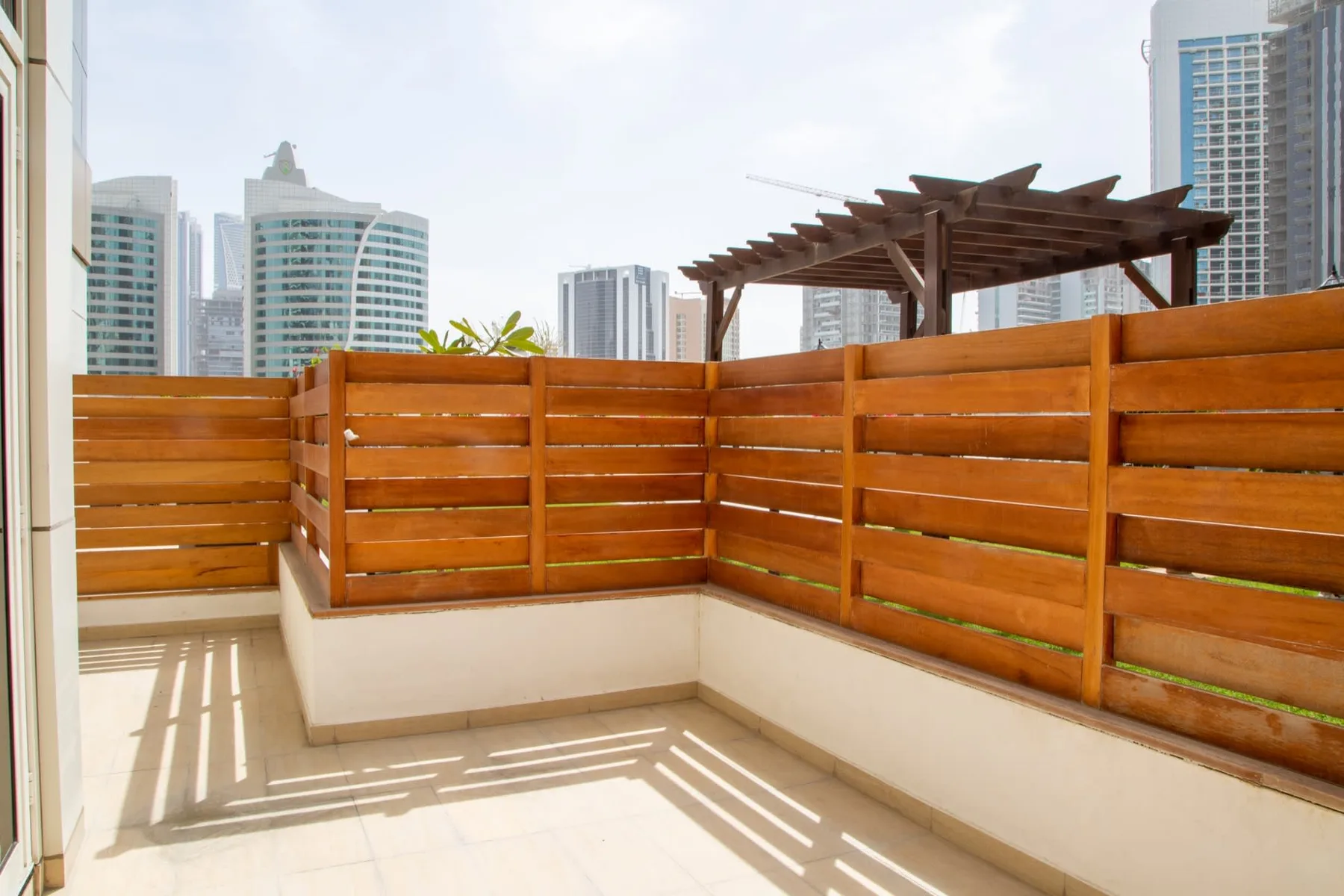 A sunlit terrace with wooden privacy screens and city buildings in the background.
