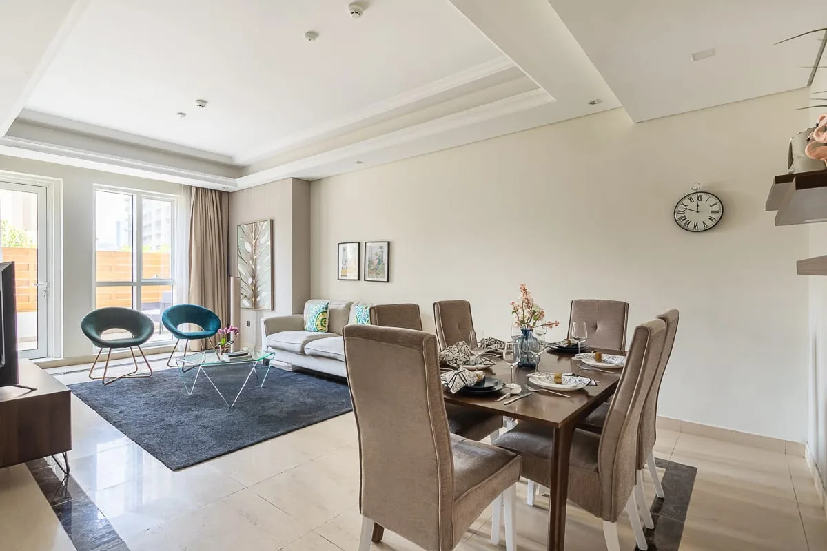 Una sala de estar y comedor con mesa, asientos y ventanas grandes.