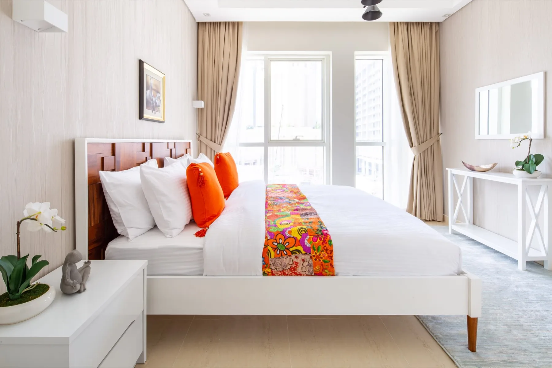 A bright bedroom with a neatly made bed and colorful patterned runner.