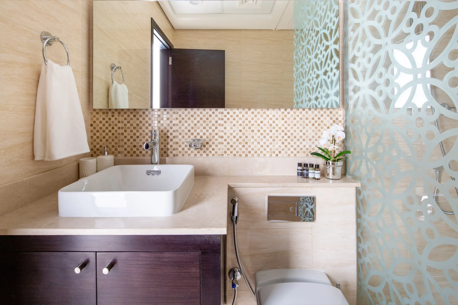 A bathroom vanity with a white basin and patterned tile backsplash.