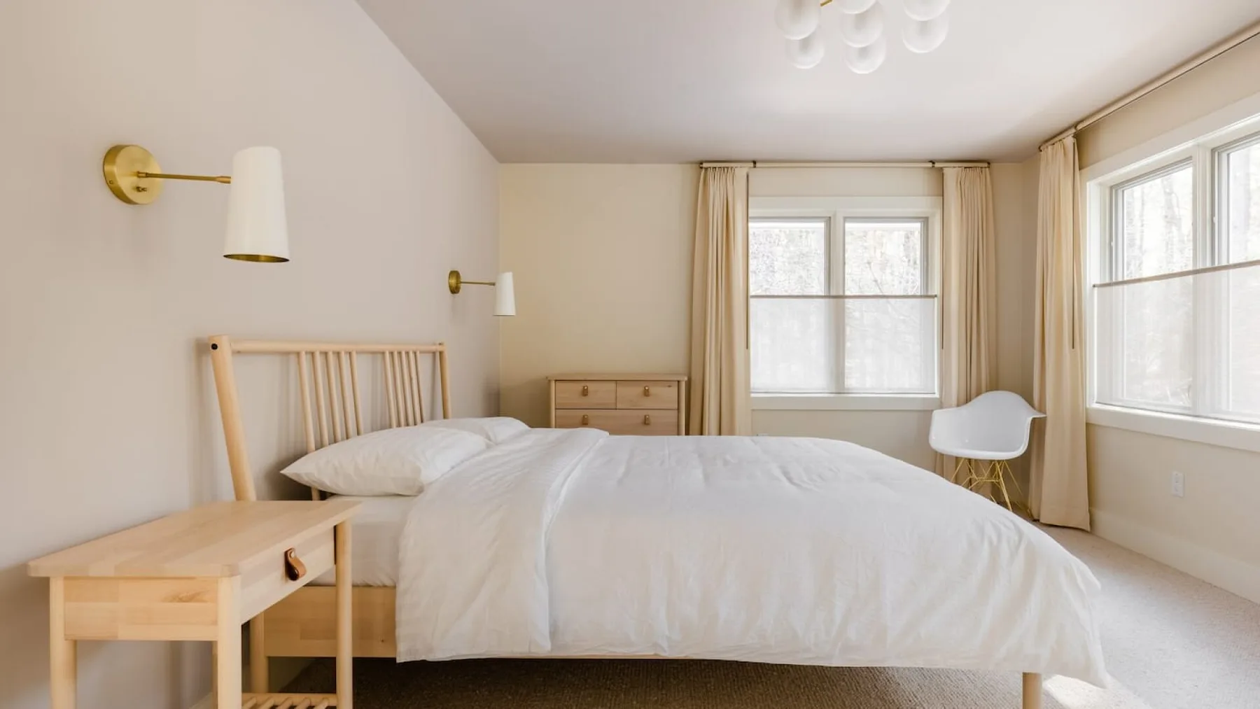Un dormitorio luminoso con una cama, muebles de madera clara y ventanas grandes.