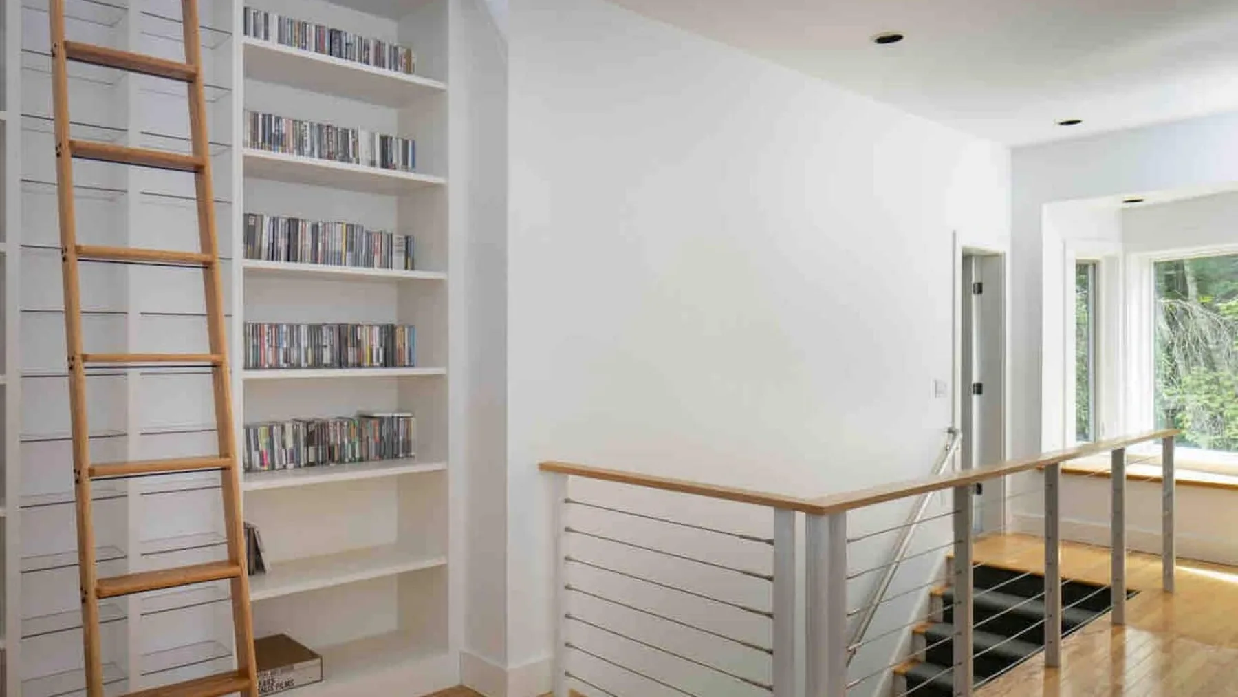 Un luminoso rellano interior con una estantería alta y una barandilla de madera.
