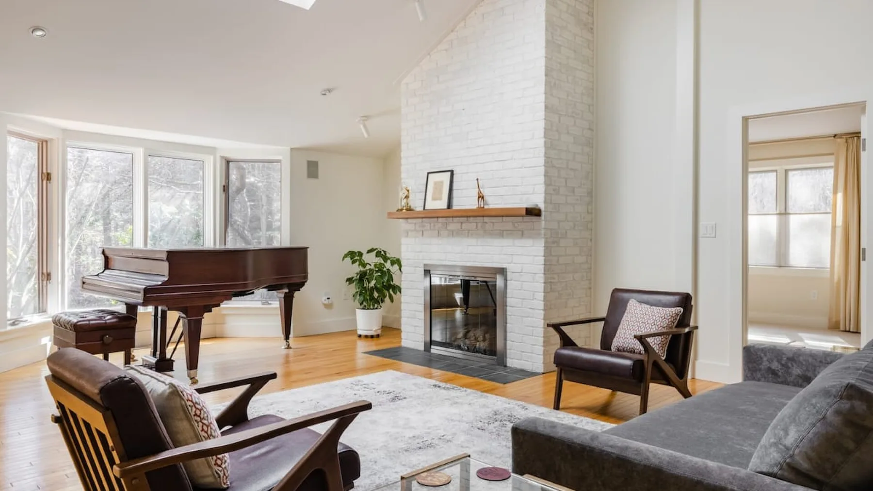 A bright living room features a piano, fireplace, and seating.