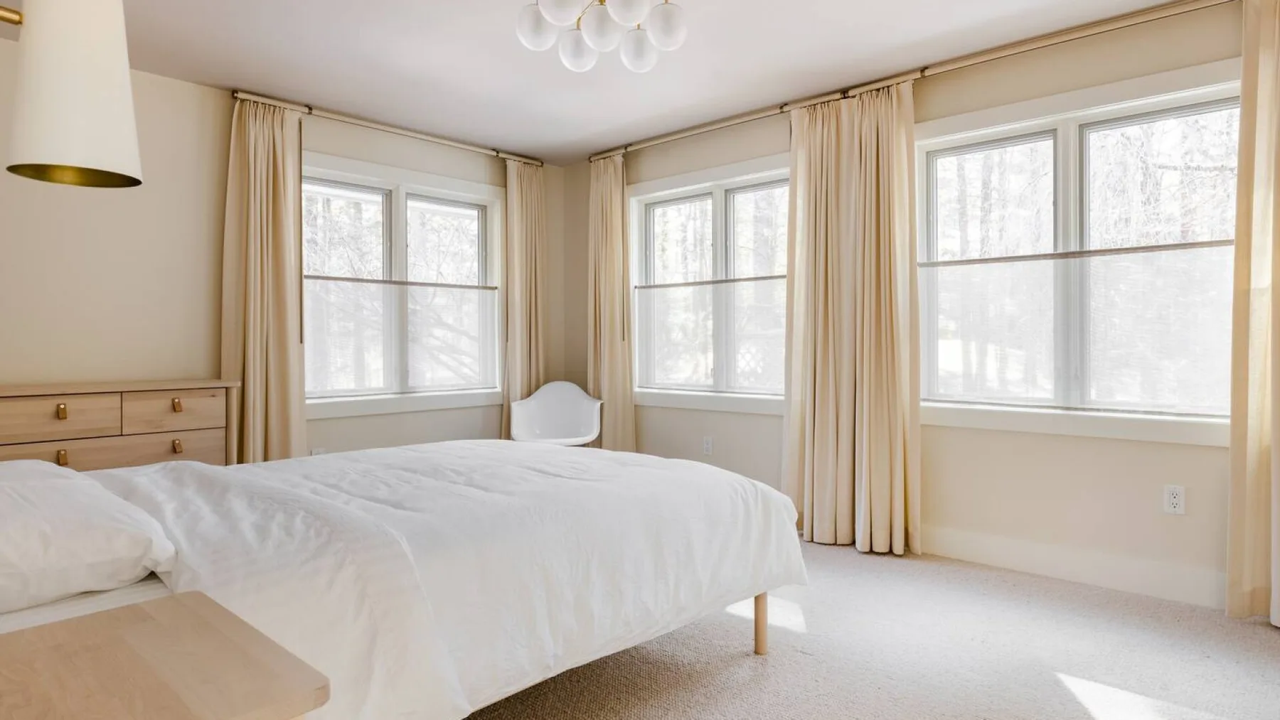 Un dormitorio luminoso con una cama y grandes ventanas con cortinas.
