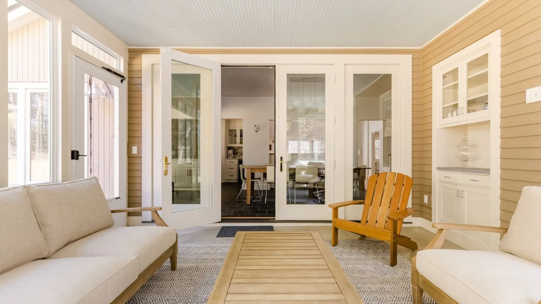 Un salón acristalado y luminoso con asientos claros y una silla de madera.