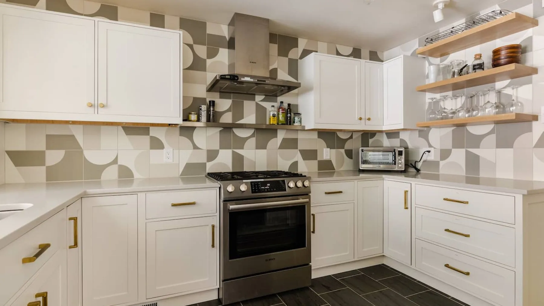 Una cocina luminosa con gabinetes blancos, estufa y estantes abiertos.