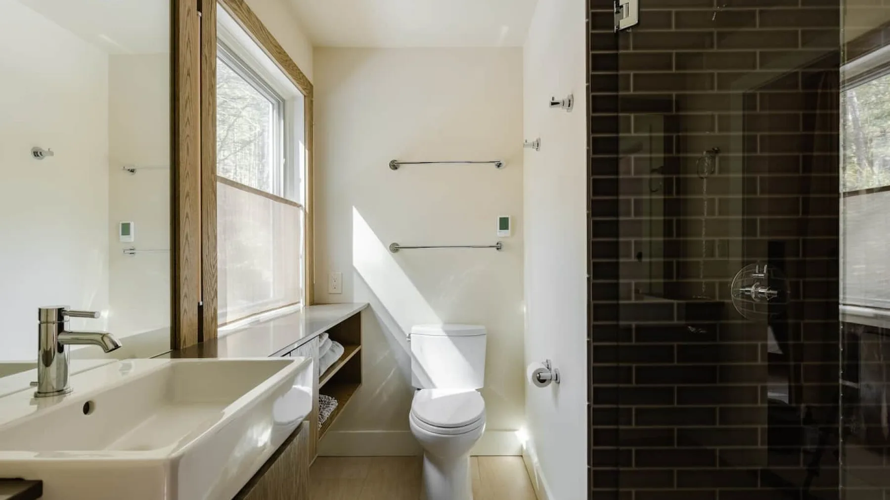 Un baño luminoso con lavabo, inodoro y una zona de ducha con azulejos oscuros.