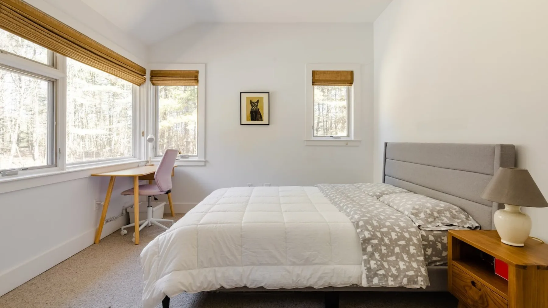 Un dormitorio luminoso con una cama bien hecha y ventanas con persianas.