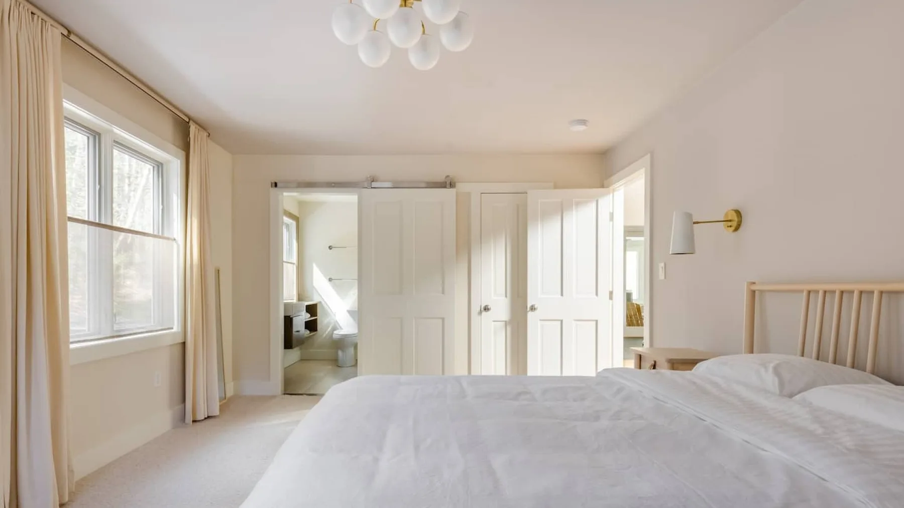 Un dormitorio luminoso con ropa de cama blanca y una ventana enmarcada por cortinas.