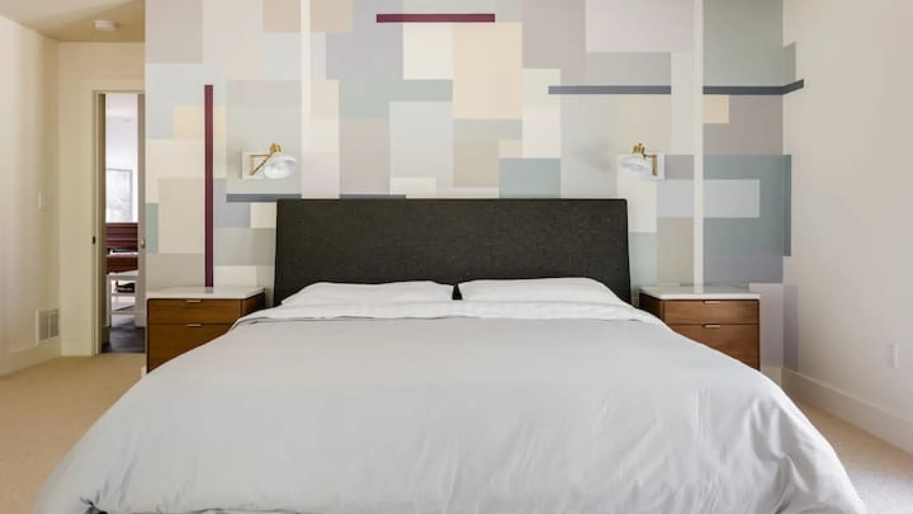 Un dormitorio con una cama bien tendida y una pared con patrones geométricos.