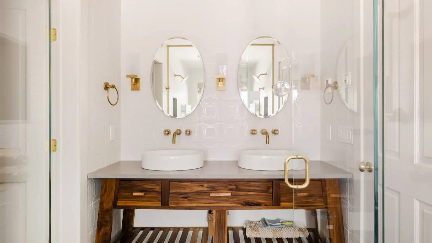 Un tocador de baño luminoso tiene dos lavabos bajo espejos ovalados.