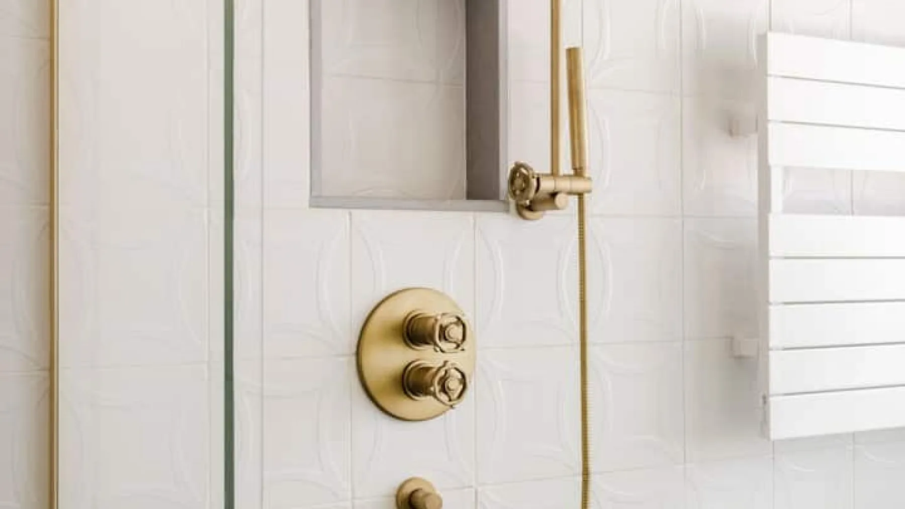 Una zona de ducha con azulejos, grifería de latón y un toallero calefactable blanco.