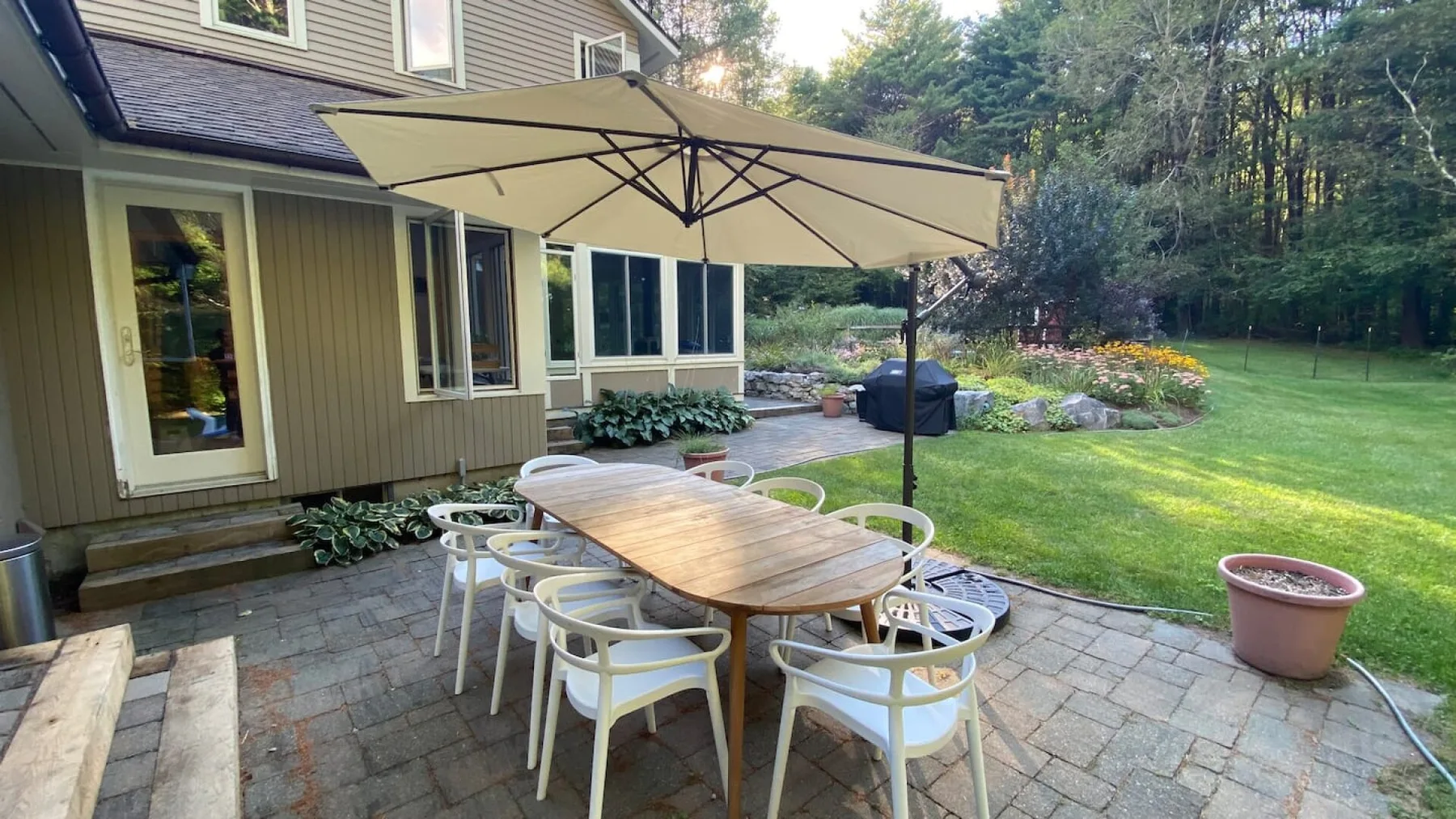 Una mesa de patio está bajo una sombrilla grande junto a un césped verde.