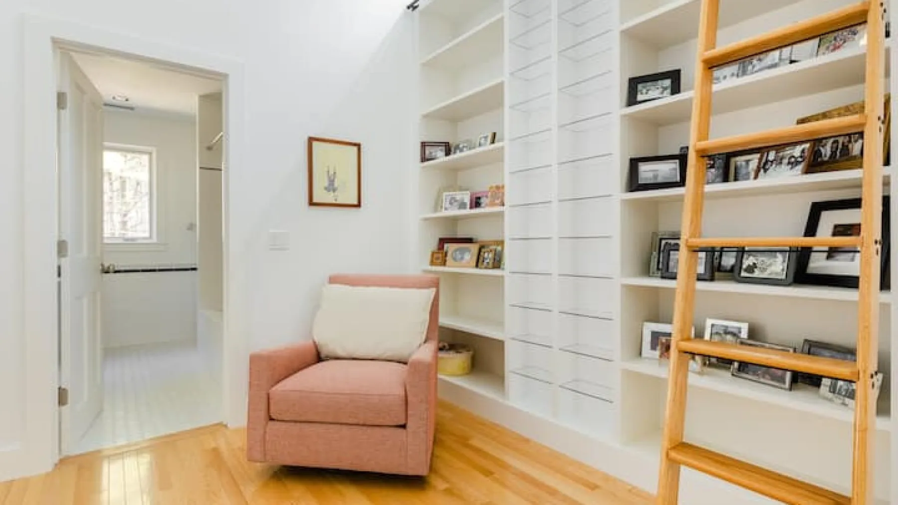 Una luminosa zona de estar con un sillón junto a estantes empotrados y una escalera de madera.