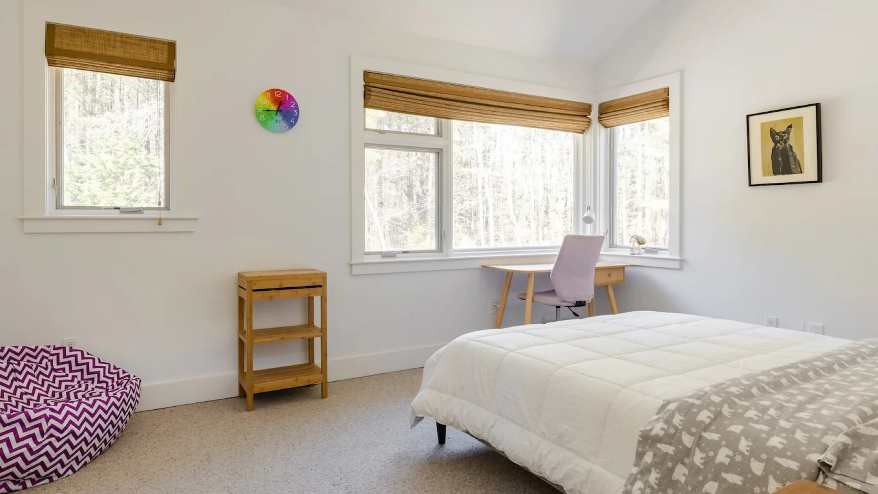 Un dormitorio luminoso con una cama, un escritorio y ventanas grandes.