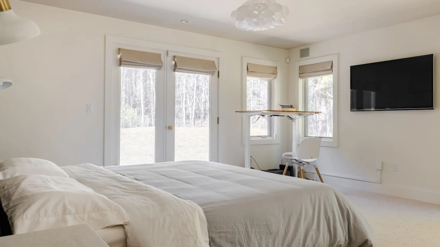 Un dormitorio luminoso con una cama, ventanas y un televisor montado en la pared.