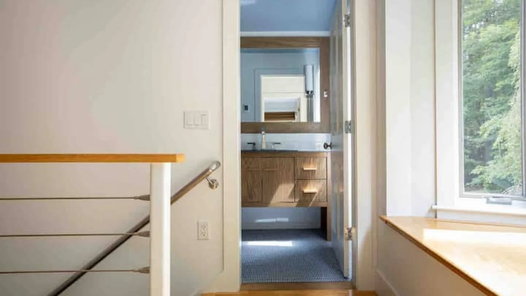 Se ve un lavabo con espejo a través de una puerta abierta, junto a una ventana amplia.