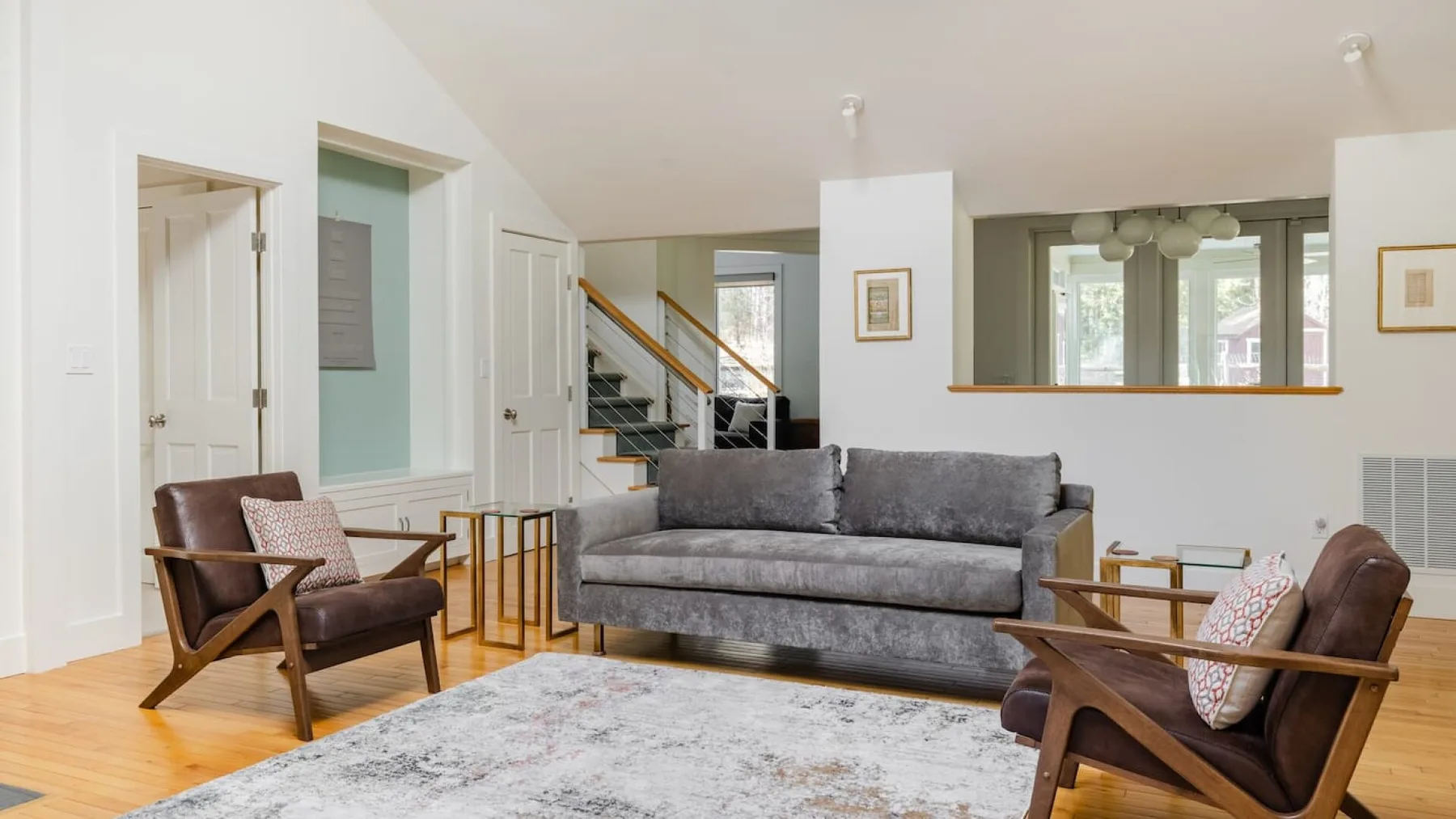 A bright living room with a gray sofa, wooden chairs, and a large area rug.