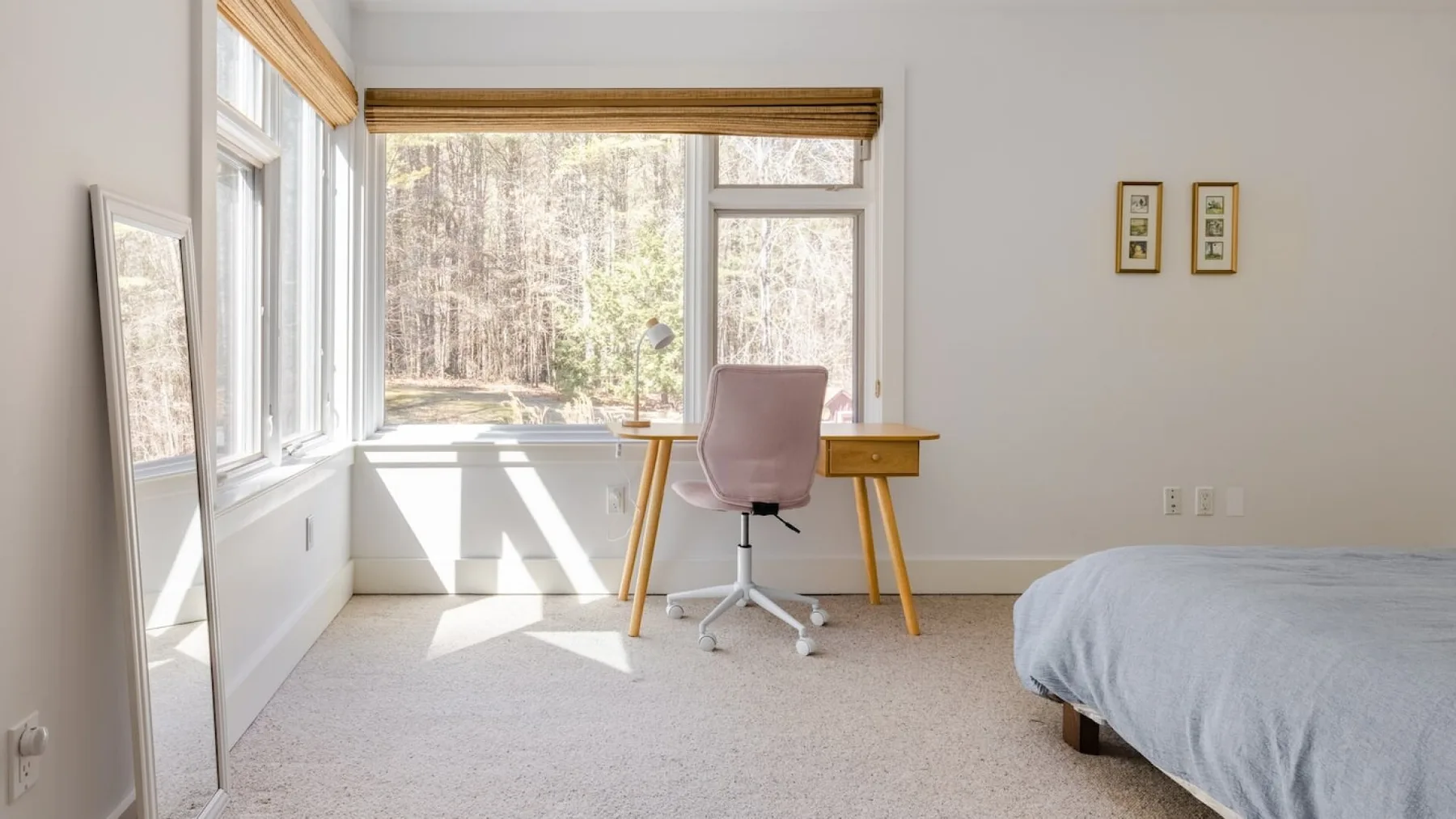 Un dormitorio luminoso con un escritorio junto a grandes ventanas.