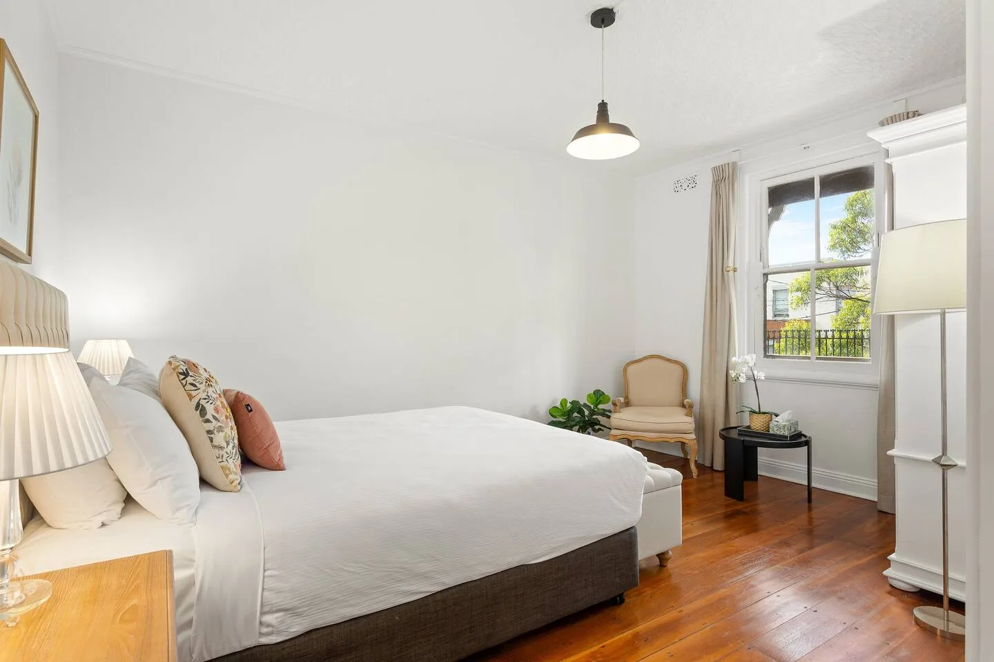 A bright bedroom with a large bed, an armchair, and a window overlooking greenery.