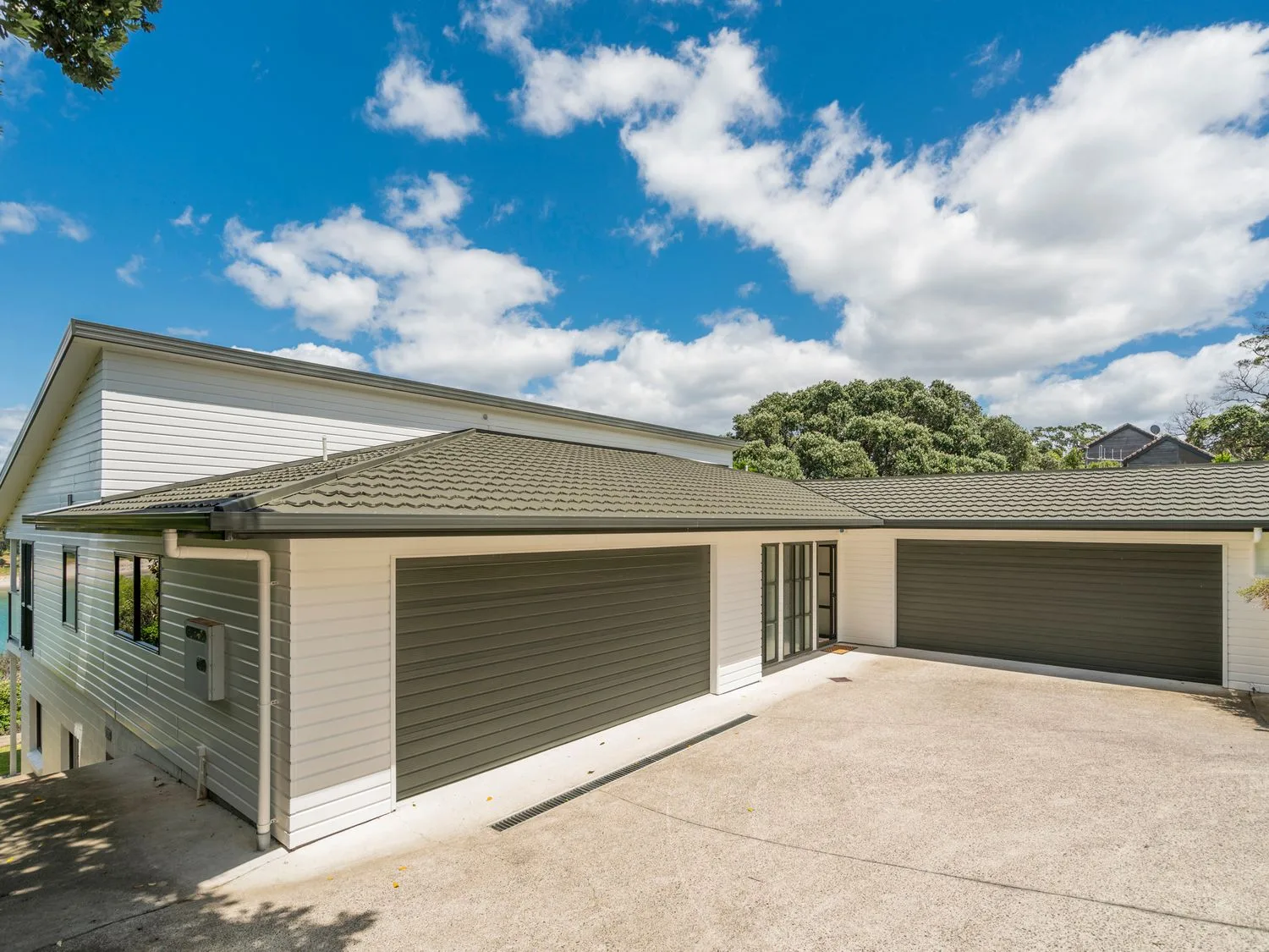 El exterior de una casa con dos grandes puertas de garaje y una entrada para vehículos bajo un cielo azul en Pohutukawa on Paku - Tairua Holiday Home, en Tairua.