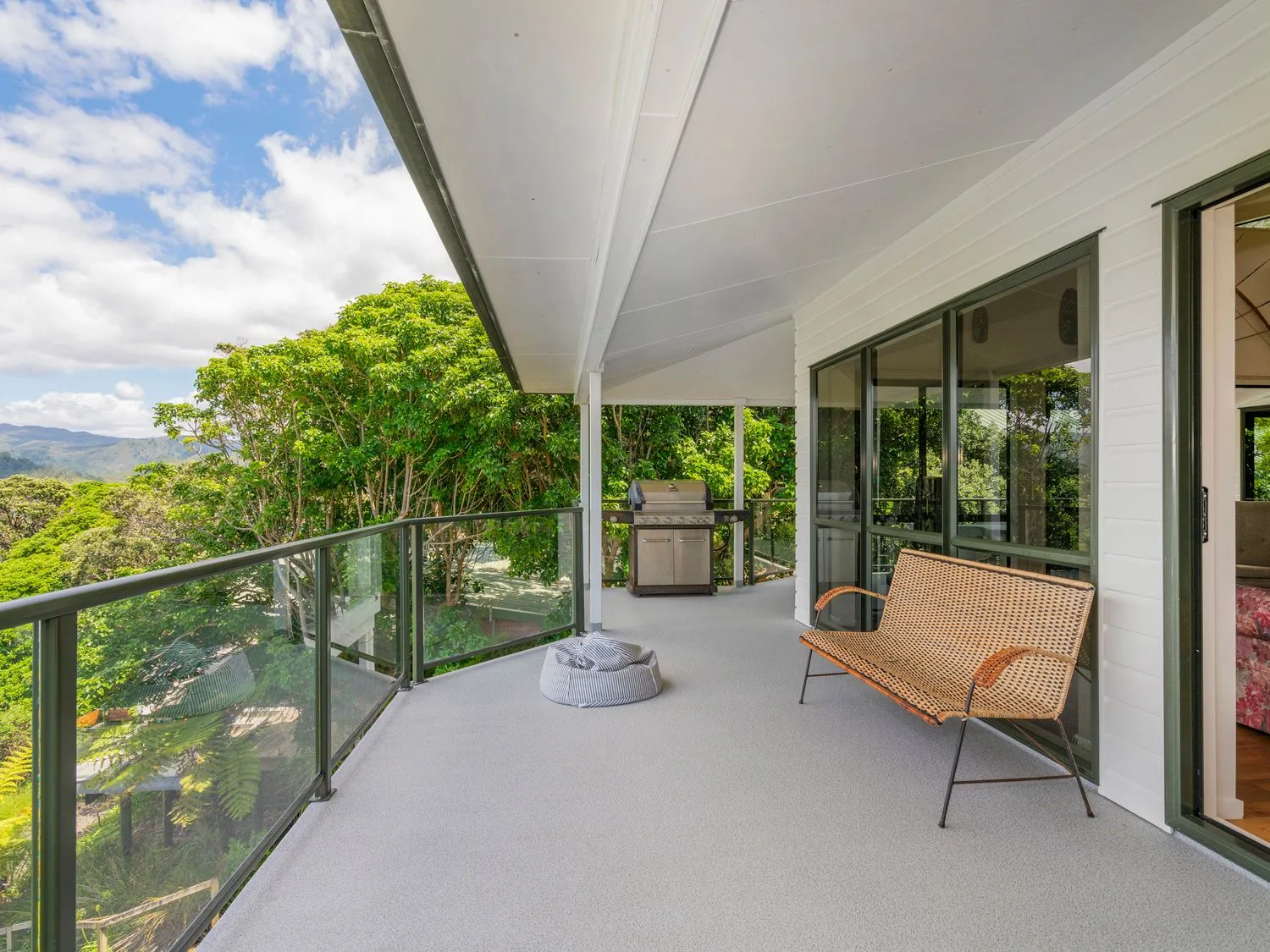 Un balcón exterior con un banco, una parrilla y una barandilla de vidrio con vistas a los árboles en Pohutukawa on Paku - Tairua Holiday Home, en Tairua.