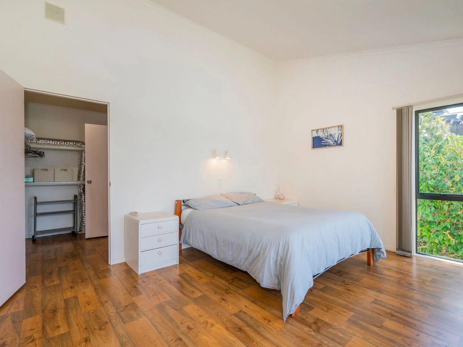 Un dormitorio con una cama, una cómoda y un armario abierto.