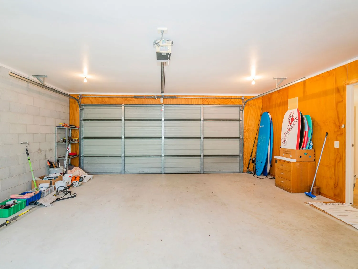 Un garaje con la puerta cerrada, tablas de surf guardadas y utensilios de limpieza.