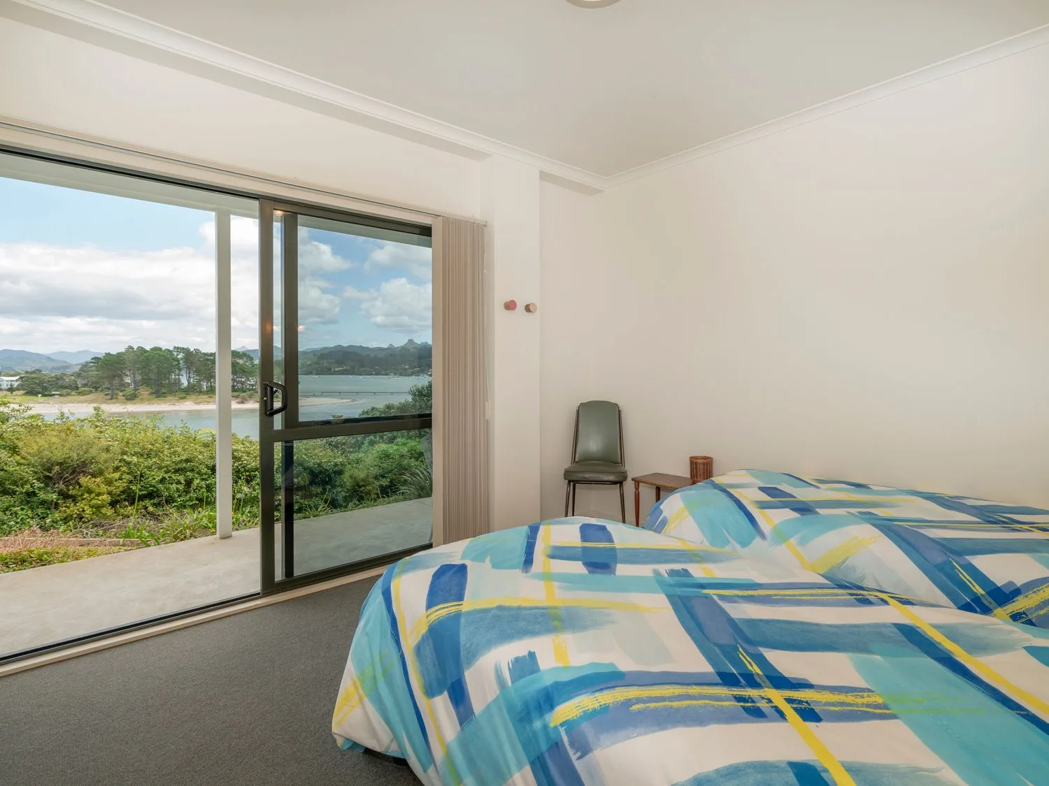 Un dormitorio con dos camas junto a una puerta corredera de vidrio con vistas al exterior en Pohutukawa on Paku - Tairua Holiday Home, en Tairua.