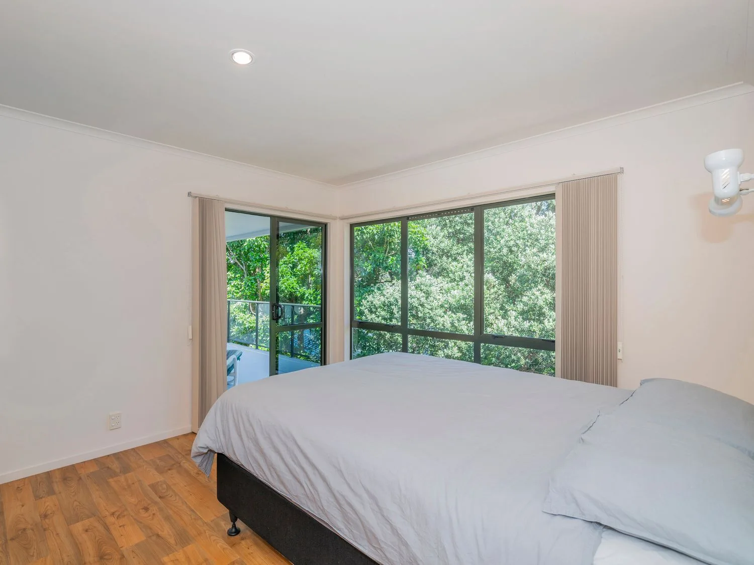 Un dormitorio con una cama junto a grandes ventanas que dan a una vegetación frondosa.