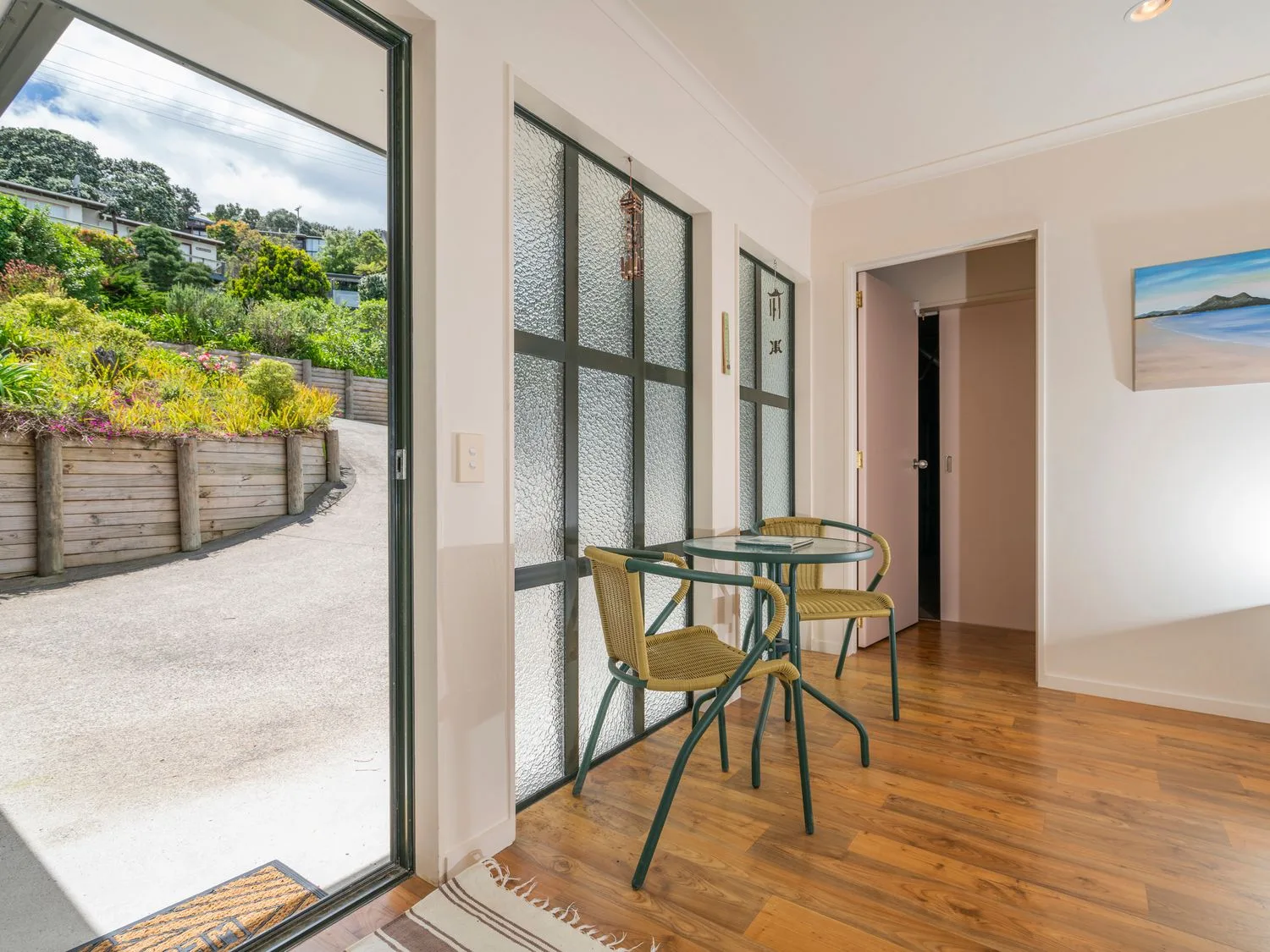Una zona de comedor con una mesa de vidrio y sillas junto a paneles de vidrio texturizado y una puerta abierta.