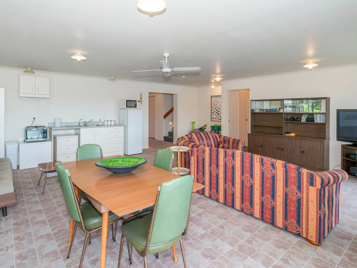 Una zona combinada de sala y comedor tiene una mesa de madera, asientos verdes y sofás a rayas.