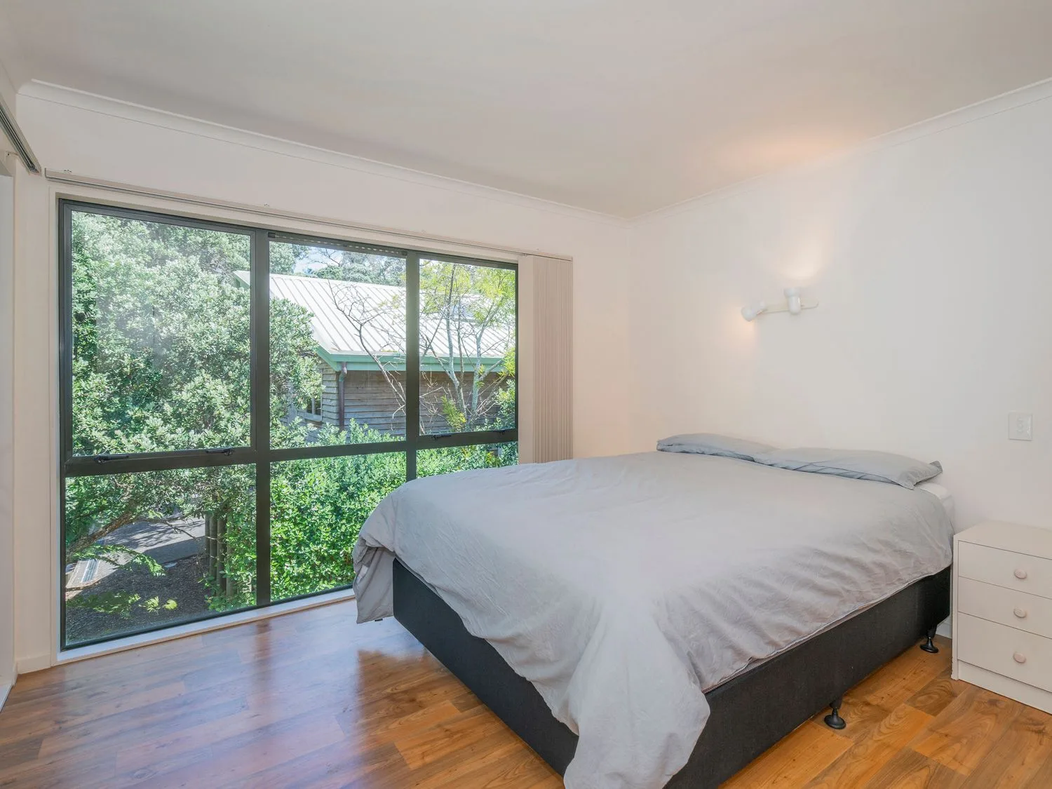 Un dormitorio con una cama junto a una ventana grande con vistas a la vegetación.