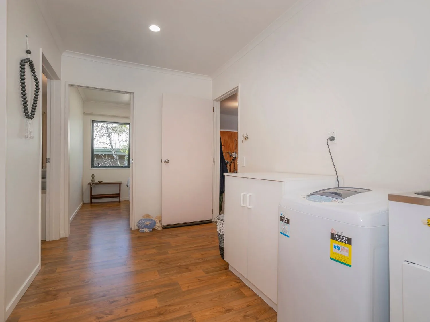 Un cuarto de lavado con una lavadora, armarios blancos y suelo de madera en Pohutukawa on Paku - Tairua Holiday Home, en Tairua.