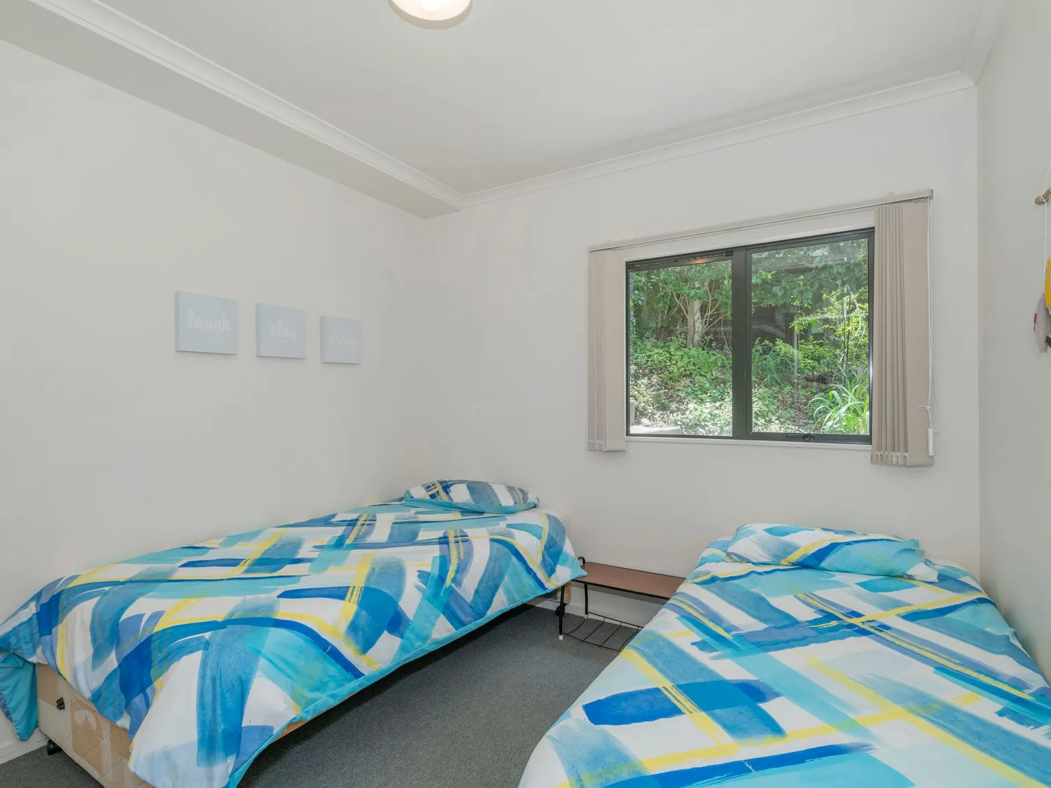 Un dormitorio con dos camas individuales con colchas azules estampadas y una ventana que deja ver la vegetación exterior en Pohutukawa on Paku - Tairua Holiday Home, en Tairua.
