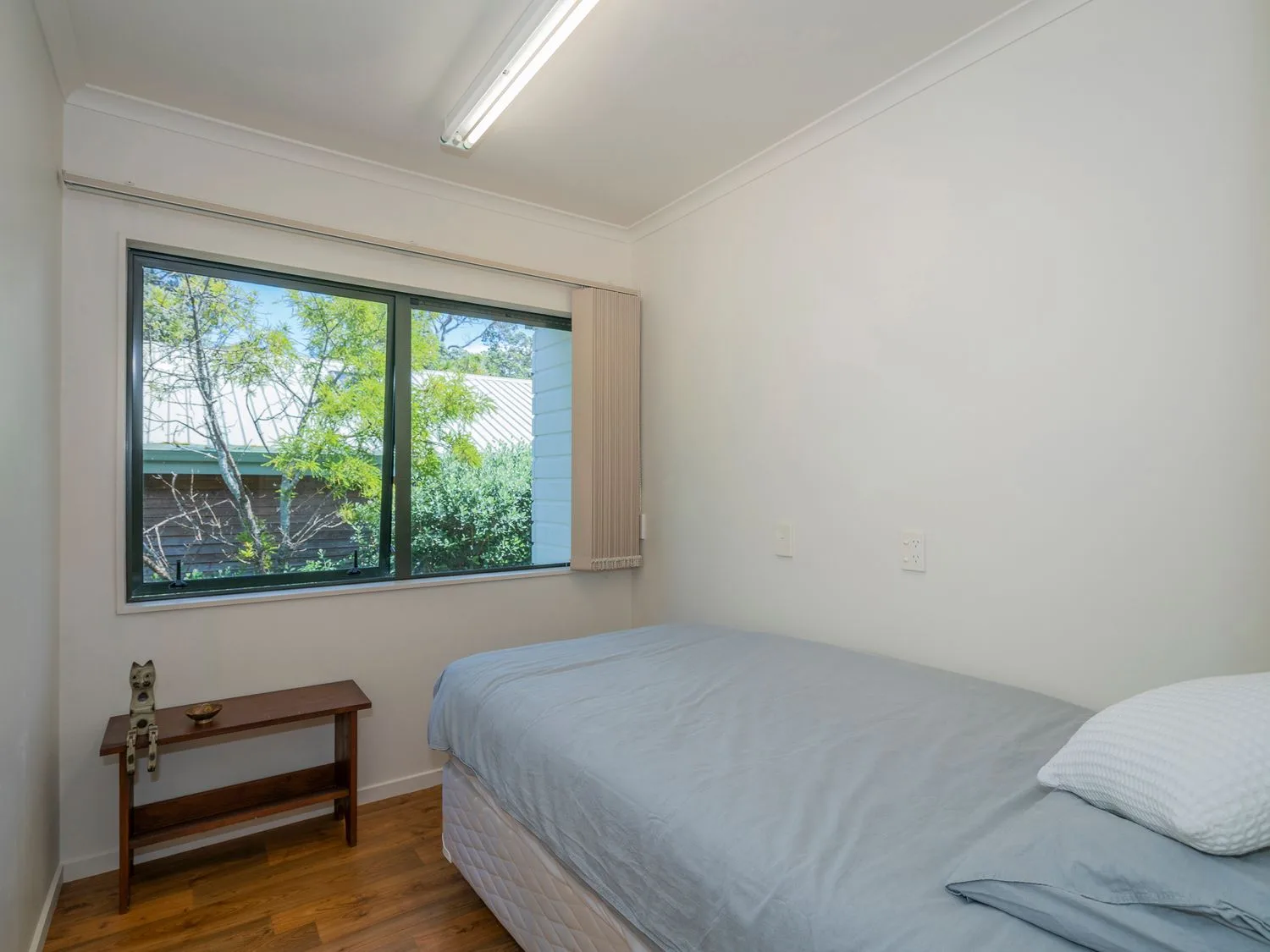 Un dormitorio pequeño con una cama individual, un banco de madera y una ventana que deja ver árboles en Pohutukawa on Paku - Tairua Holiday Home, en Tairua.