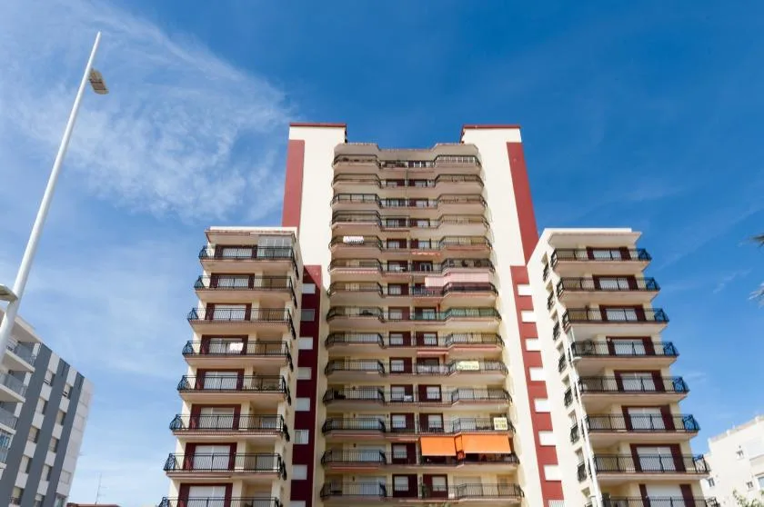 A tall apartment building with balconies rises against a clear blue sky.
