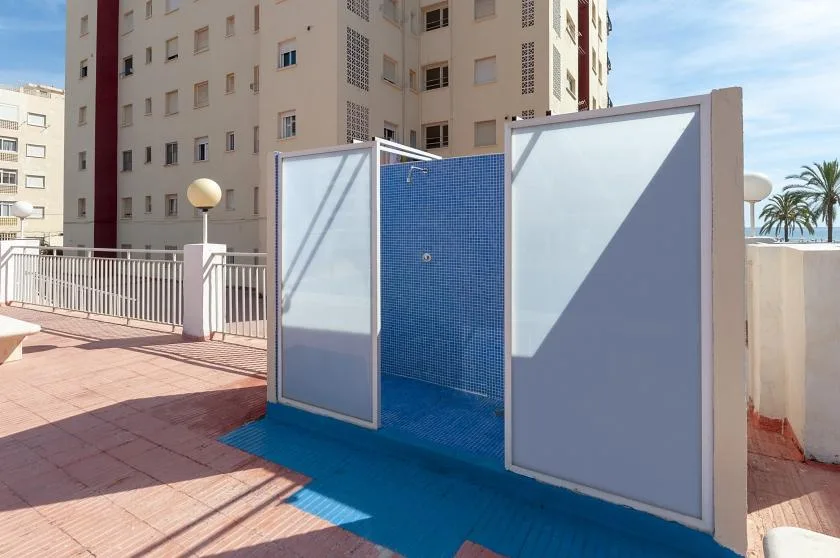 An outdoor shower with blue tile walls stands on a paved terrace.