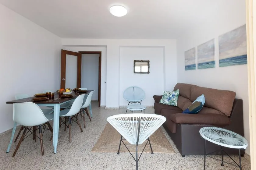 A bright living and dining area with a brown sofa and white seating.