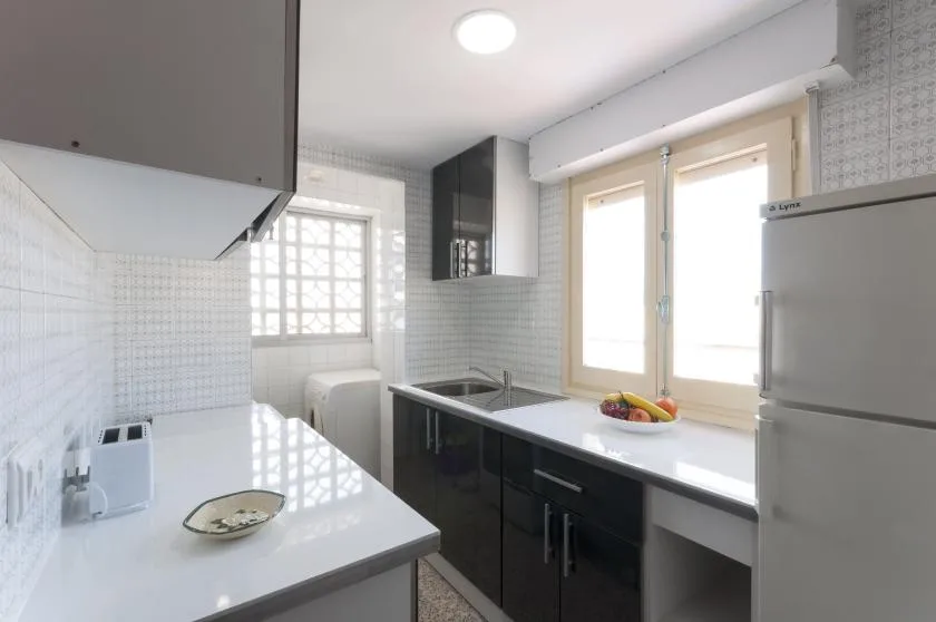 A bright kitchen with dark cabinets, white counters, and a window.