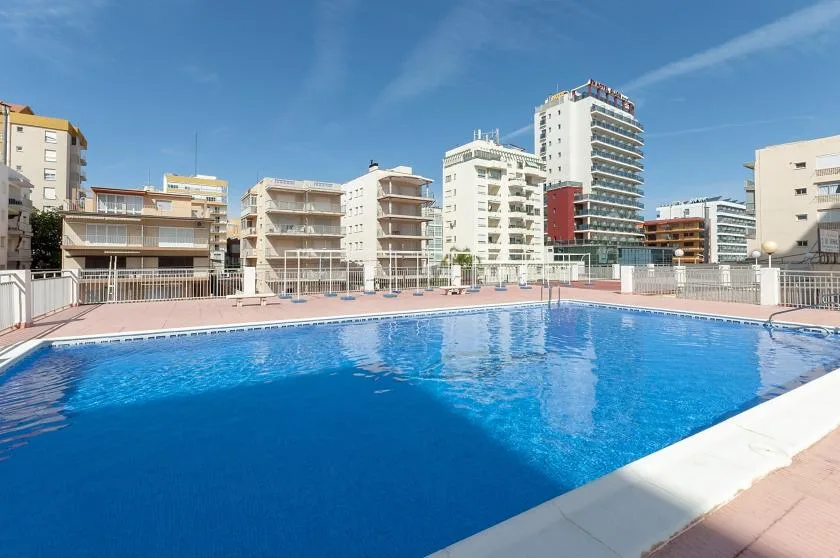 An outdoor swimming pool sits among several apartment buildings under a clear sky.