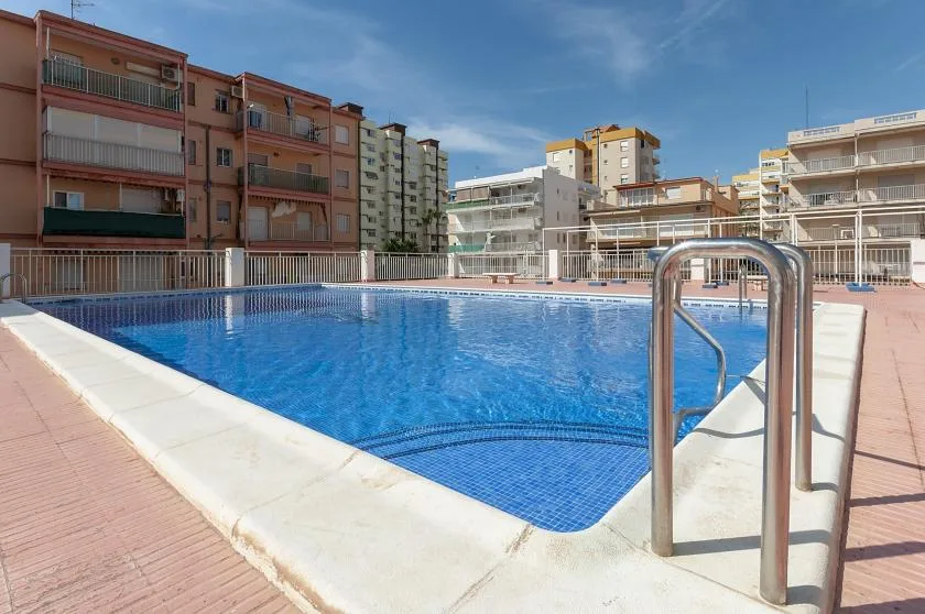 An outdoor swimming pool surrounded by apartment buildings and a paved deck.