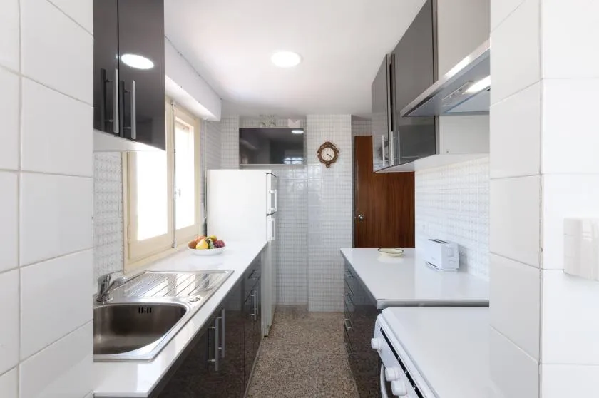 A narrow galley kitchen with counters, cabinets, and a refrigerator.